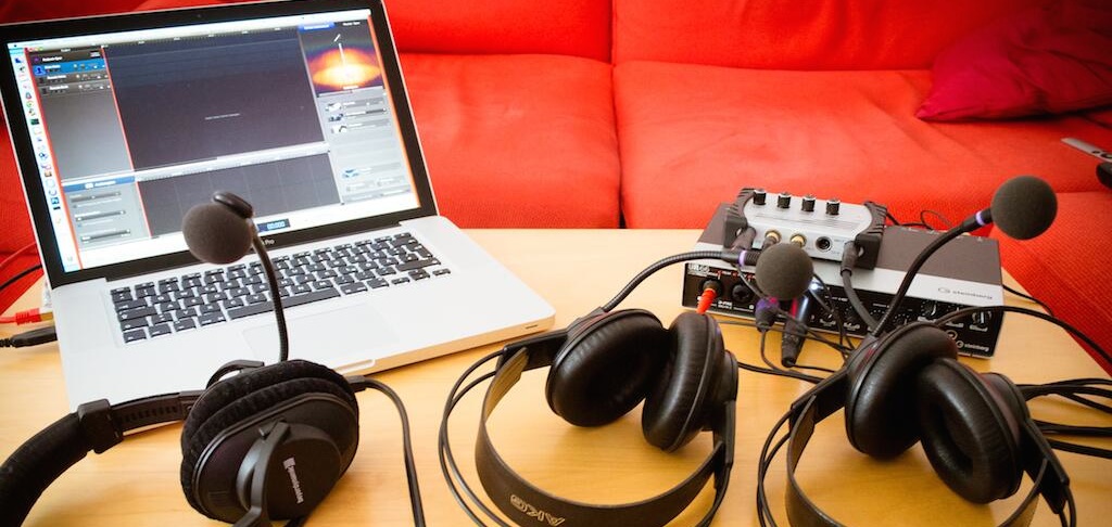  Three podcasting headphones on a table, a computer with recording software next to it. 