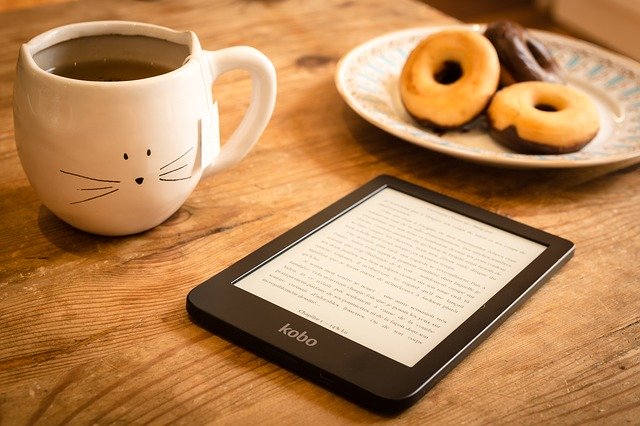  A kobo reader on a table, a cup of coffee and donuts next to it 
