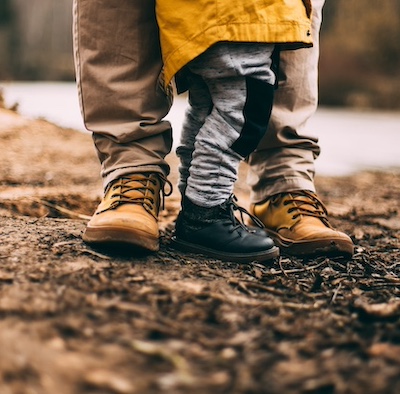  Two people standing in mud, you only see the boots of a parent and a child 
