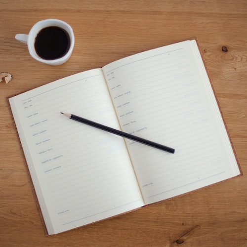  An open calendar notebook with a pencil on top of it and a cup of coffe next to it. 