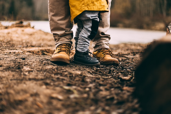  Two people standing in mud, you only see the boots of a parent and a child 