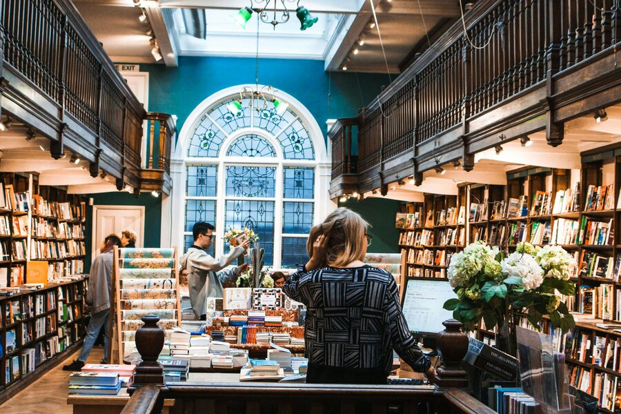  People browsing books 'Daunt Books', one of the most beautiful bookshops in London, tall shelves lined with books stretching into the background. 