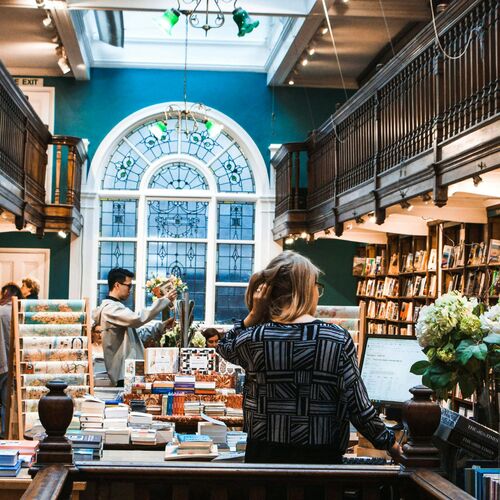  People browsing books 'Daunt Books', one of the most beautiful bookshops in London, tall shelves lined with books stretching into the background. 